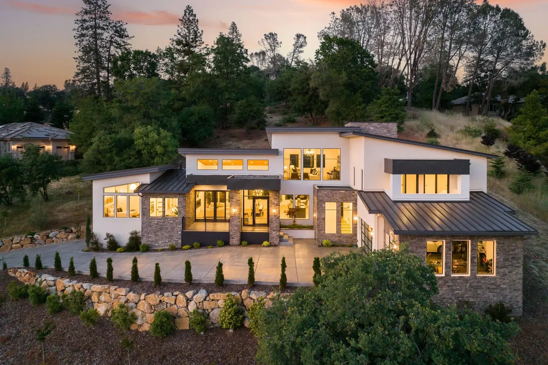 Aerial twilight view of a modern luxury home surrounded by mature trees.