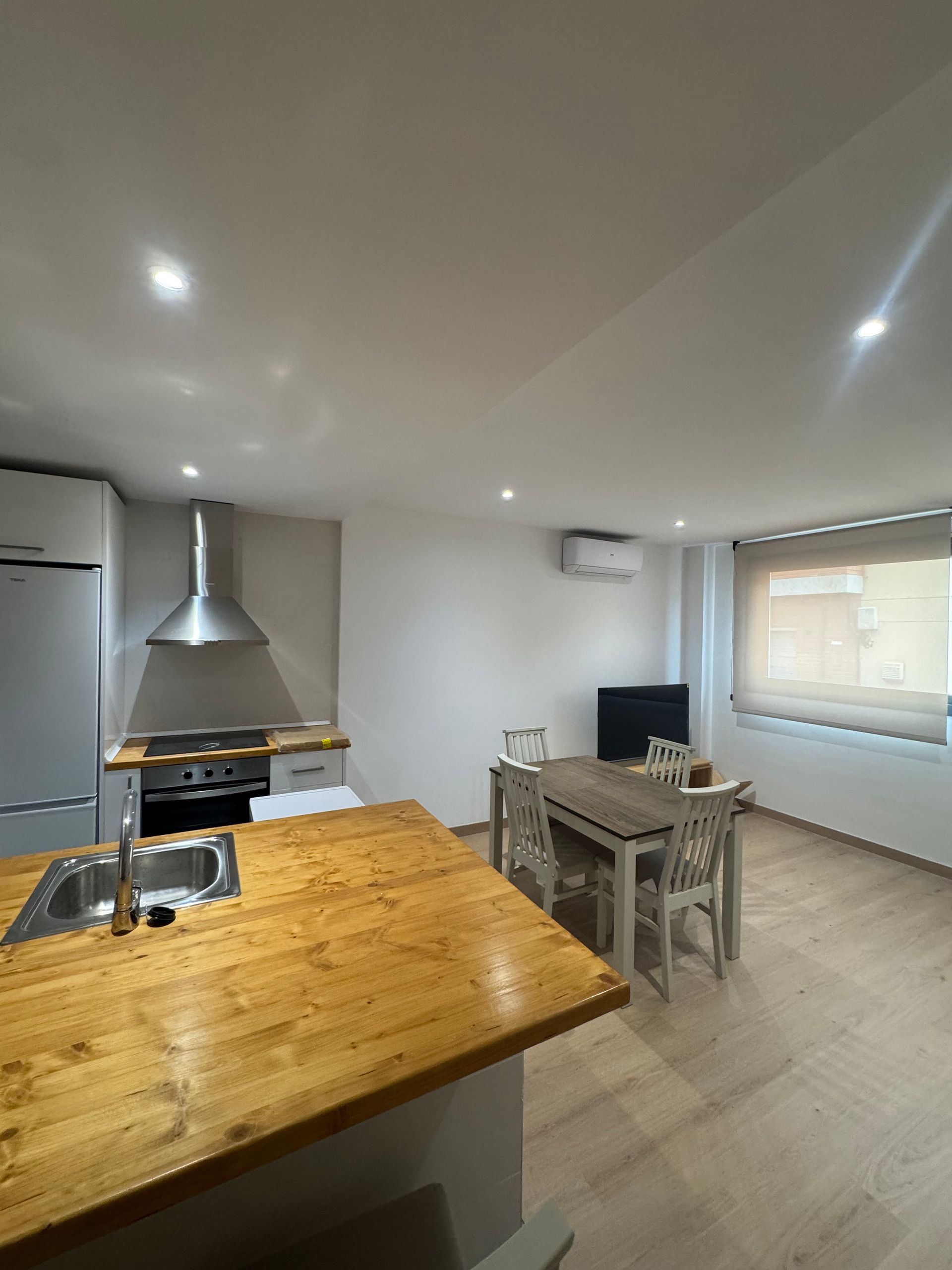 Cocina y comedor modernos con isla de madera, estufa y mesa cerca de una ventana.
