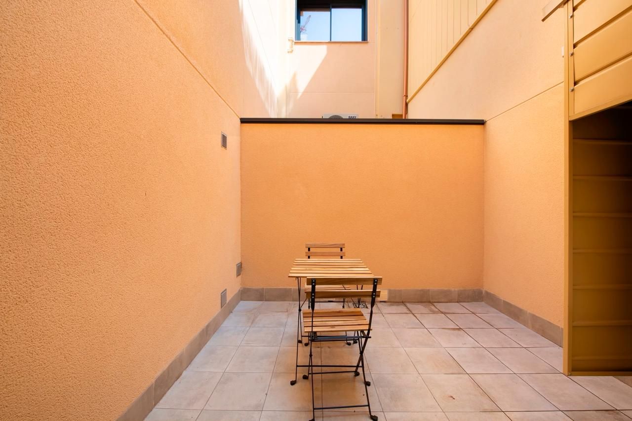 Patio al aire libre con mesa, sillas de metal, suelo de baldosas y paredes color melocotón.