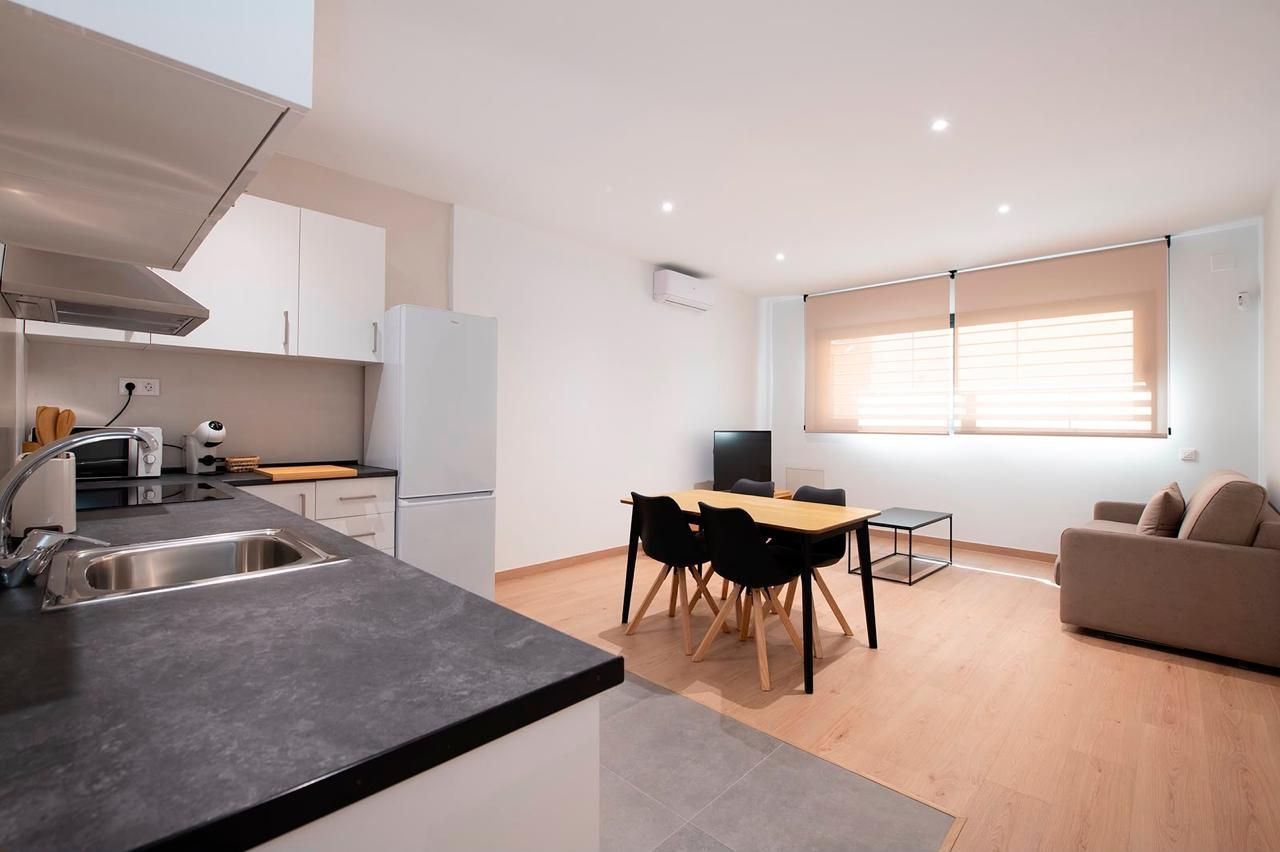 Cocina y sala de estar modernas y luminosas de planta abierta con mesa de comedor, sofá y grandes persianas.