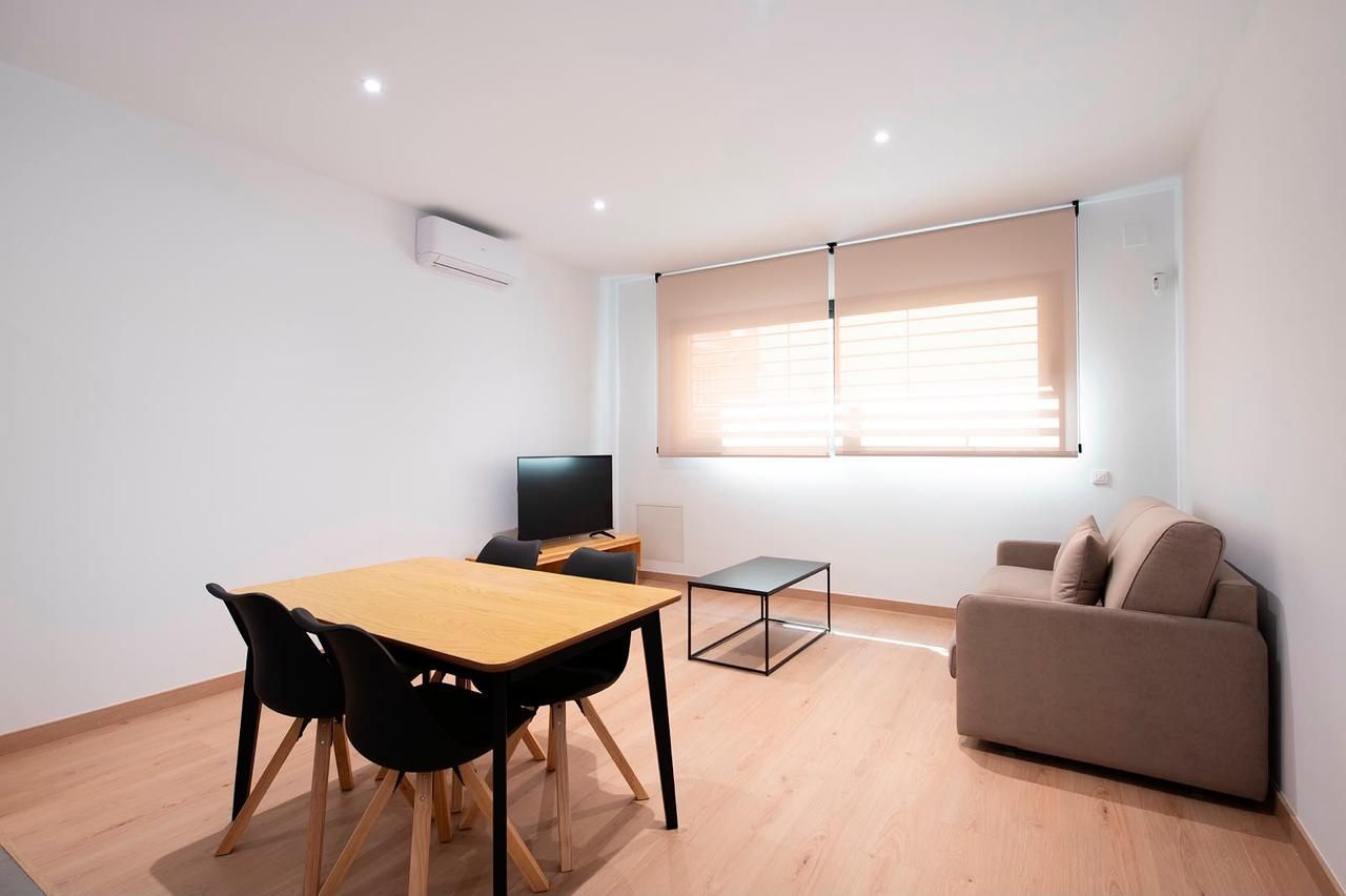 Luminoso salón moderno con mesa de comedor, televisor, sofá y gran ventanal con persianas.