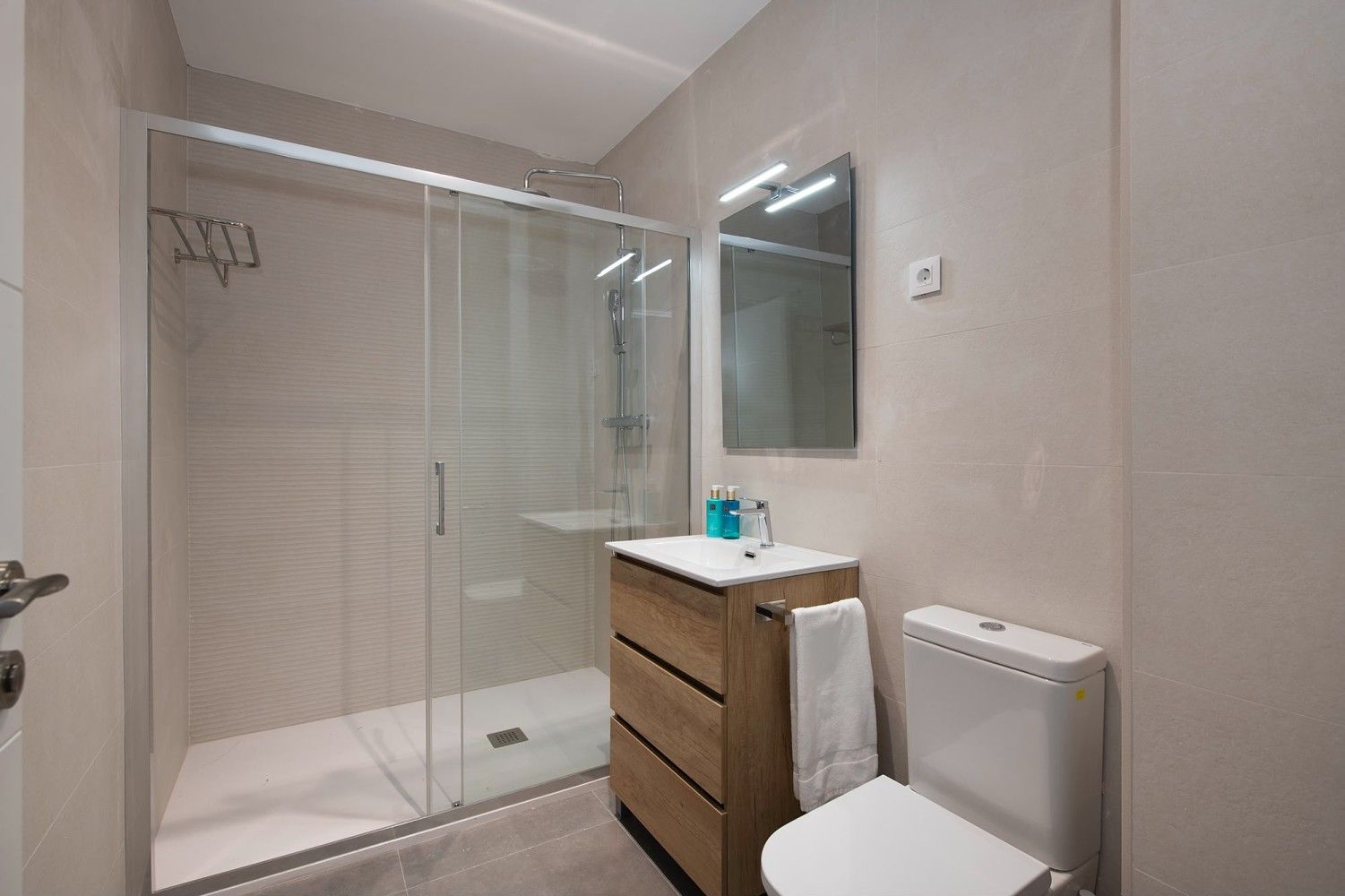 Baño moderno con ducha con mampara de cristal, lavabo de madera, espejo e inodoro.