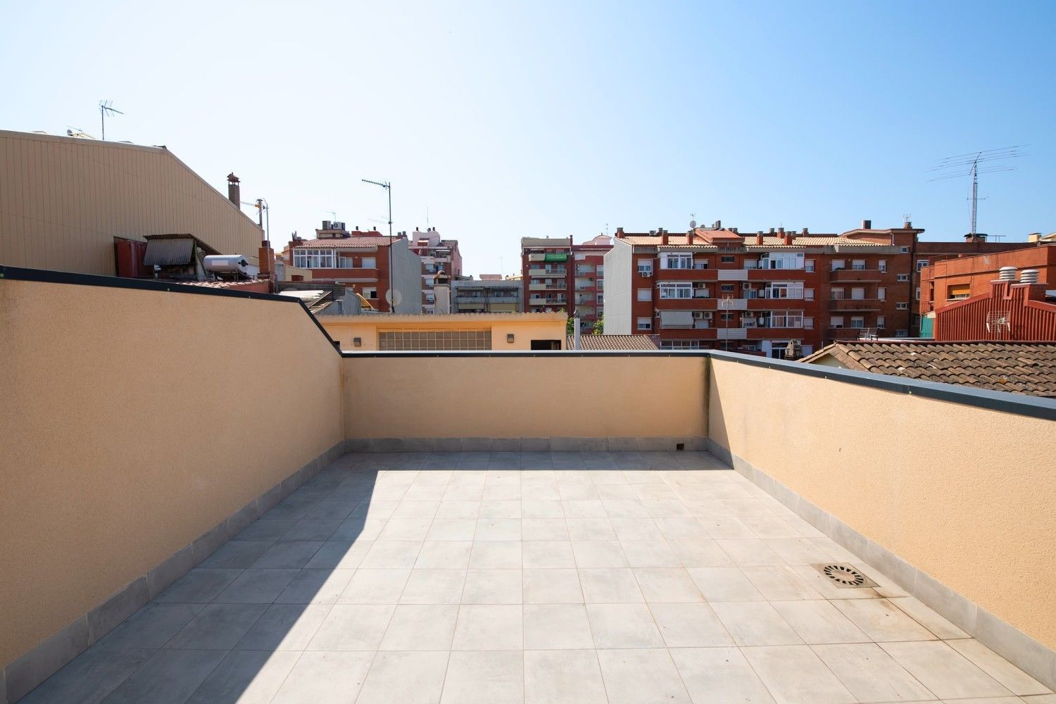 Terraza vacía en la azotea con paredes beige y edificios de la ciudad al fondo.