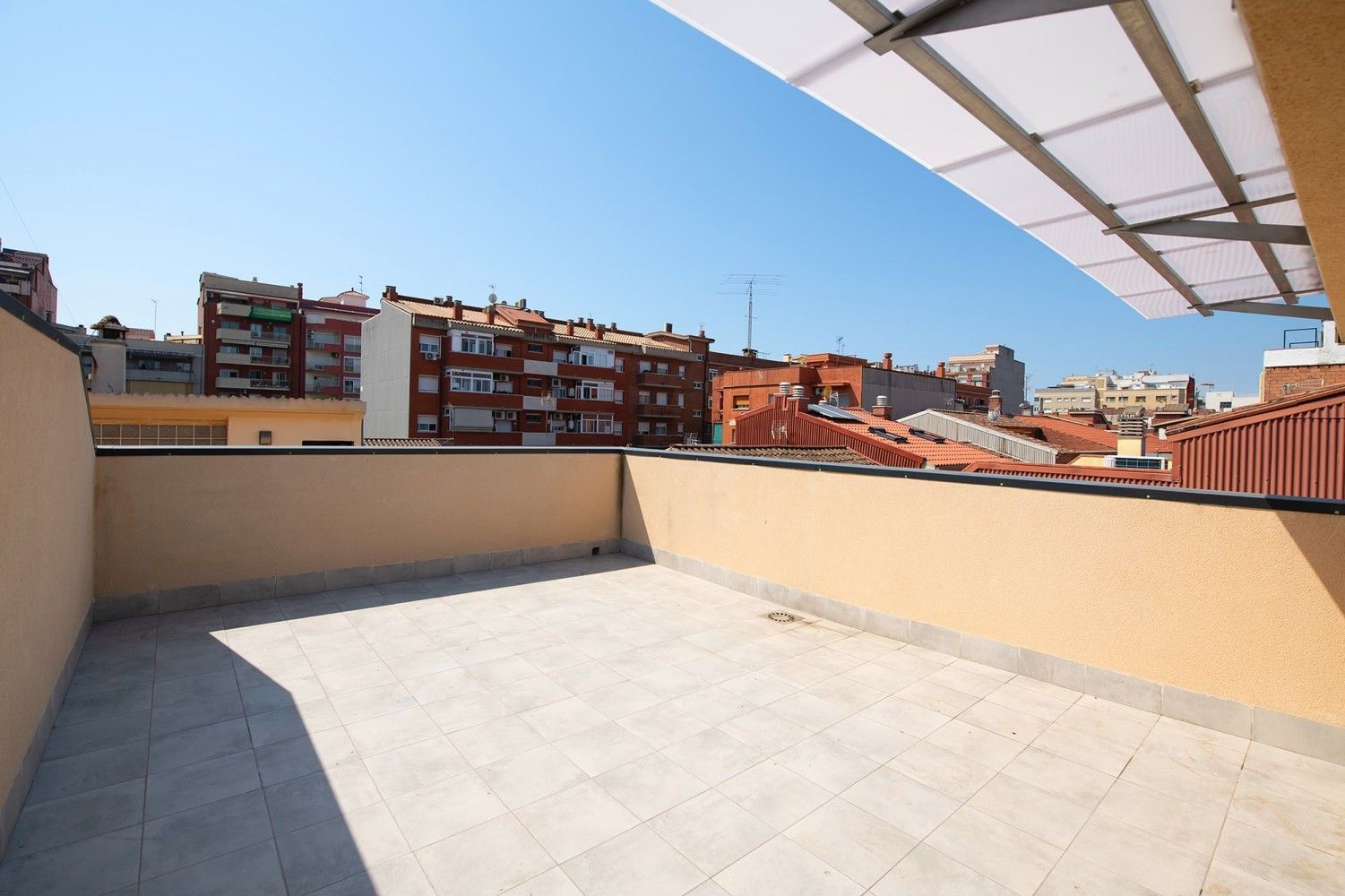 Terraza en la azotea con suelo de baldosas, paredes beige y vistas a los edificios de la ciudad.