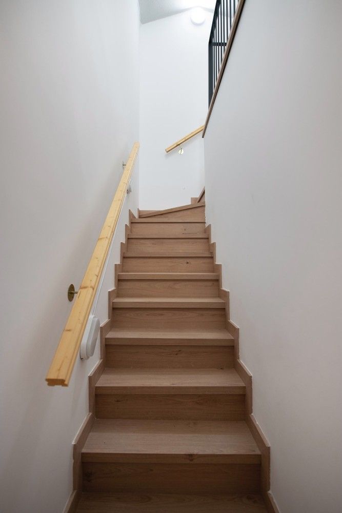 Escalera estrecha de madera con paredes y pasamanos de color claro que conduce al interior.