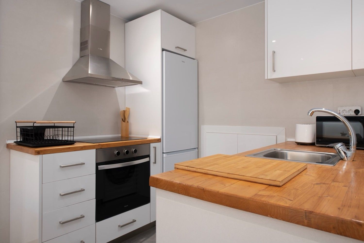 Cocina moderna blanca con electrodomésticos de acero inoxidable y encimeras de madera.