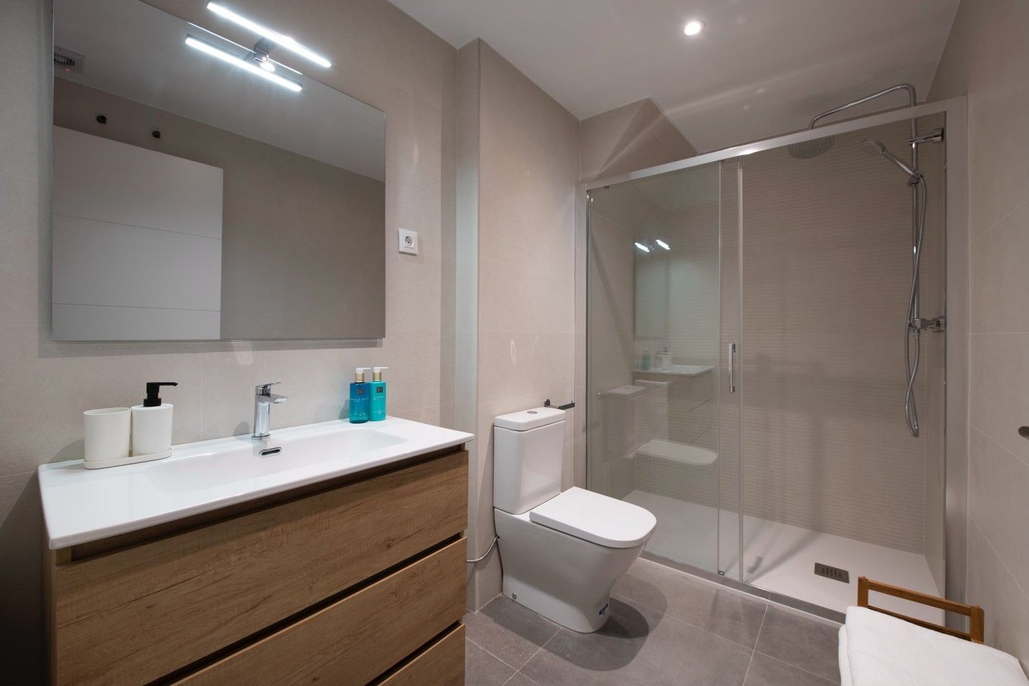 Baño moderno con lavabo doble, espejo grande, inodoro y ducha con mampara de cristal.