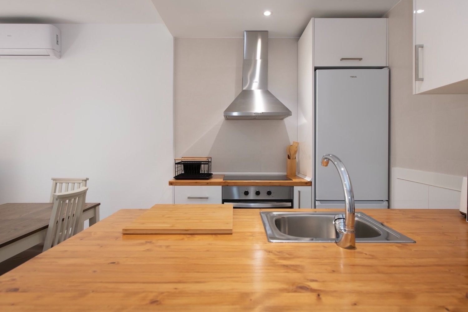 Cocina moderna con isla de madera, fregadero, campana extractora de acero inoxidable y refrigerador.