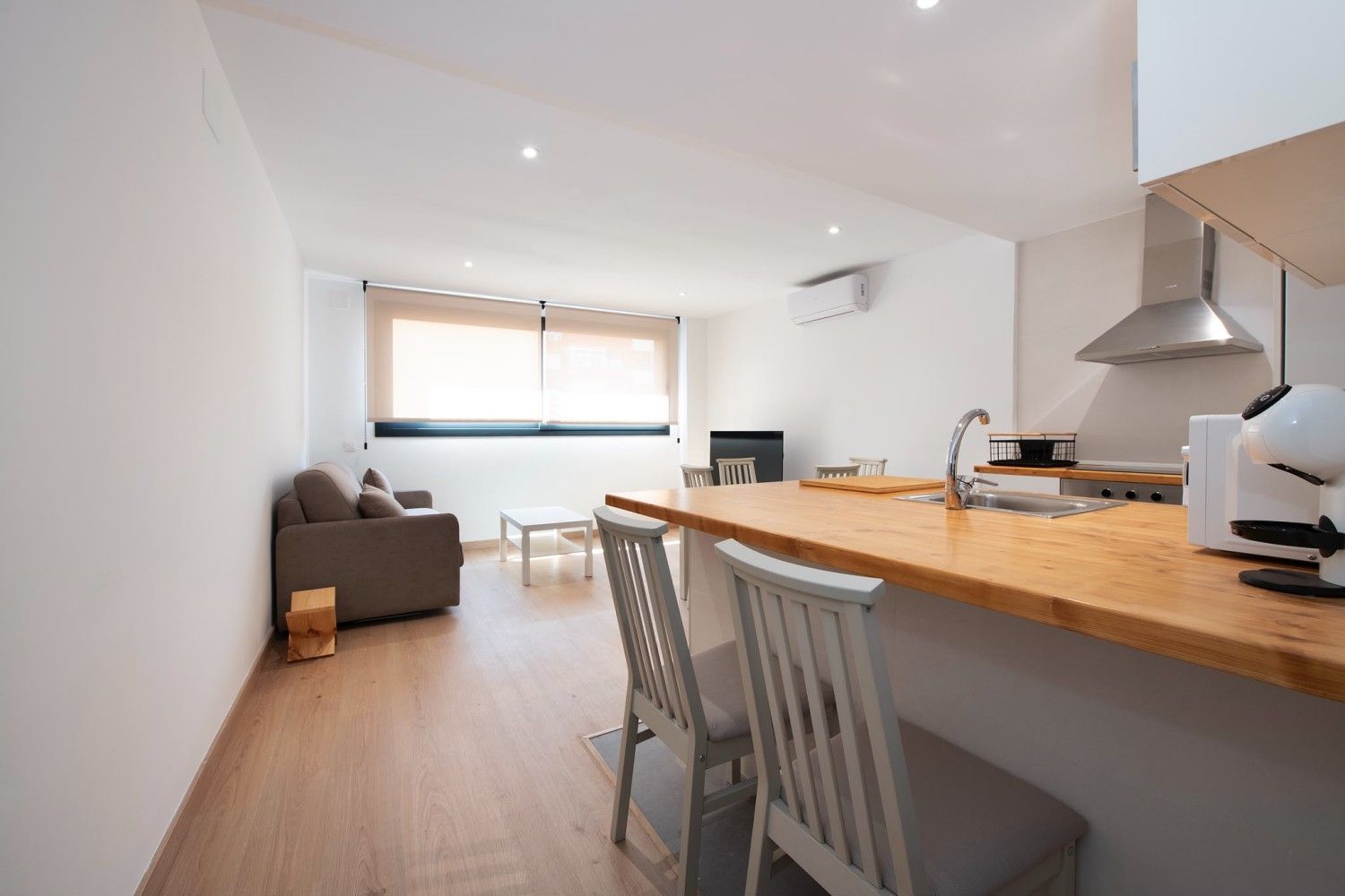 Luminosa cocina y sala de estar de planta abierta con isla de madera, sofá gris y gran ventanal.