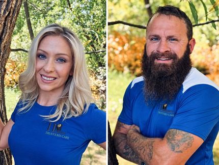 Two people in blue shirts posing outdoors in front of trees, smiling at the camera.