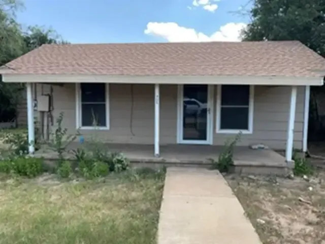 Small beige house with a front porch, white columns, and a concrete walkway leading to the door.