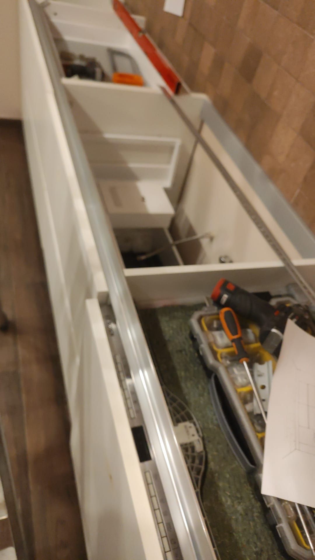Cassetto aperto con organizer bianchi, attrezzi e componenti metallici su un pavimento in legno.