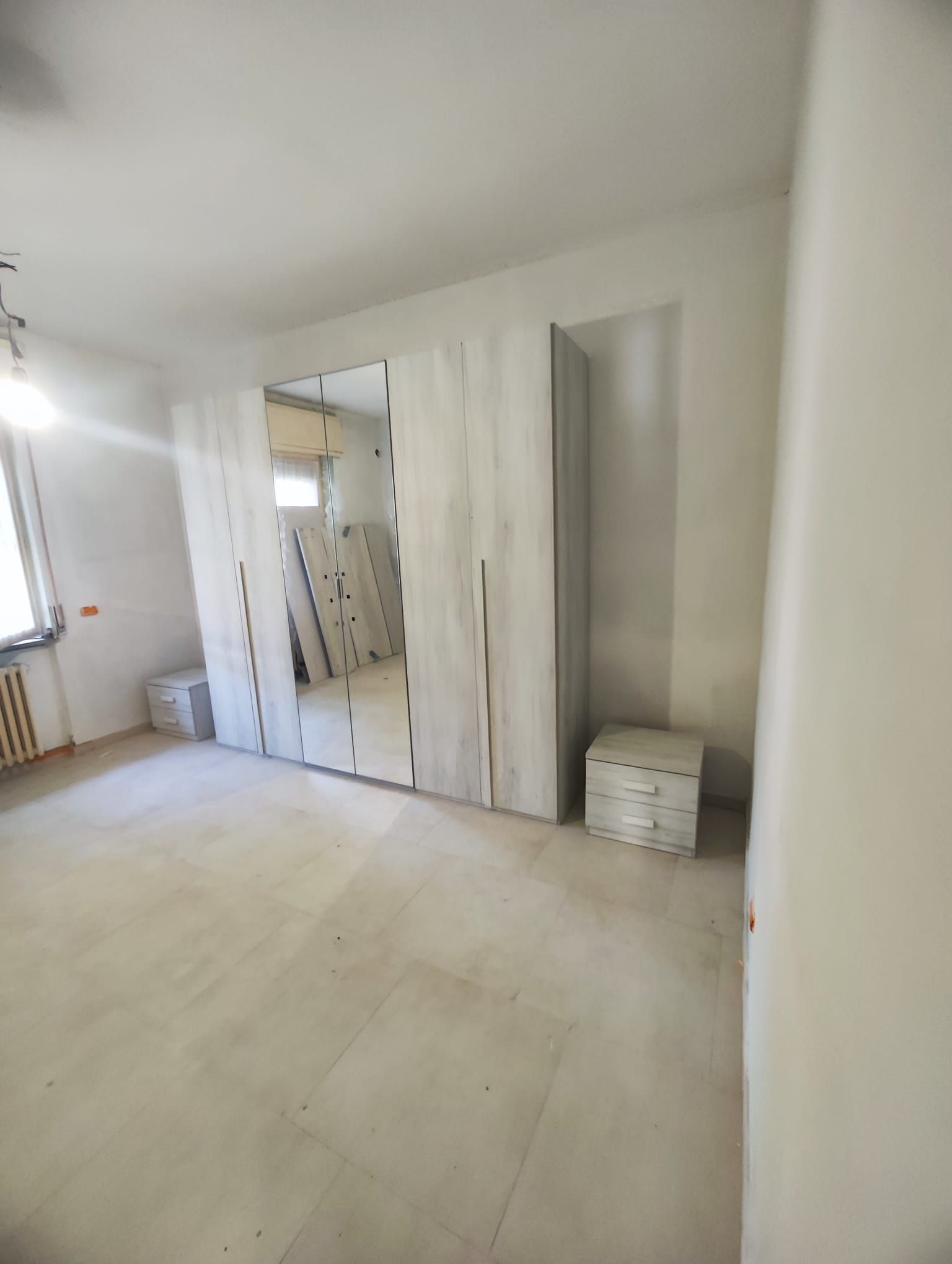 Luminosa stanza vuota con pareti bianche, armadio a specchio e piastrelle beige sul pavimento.