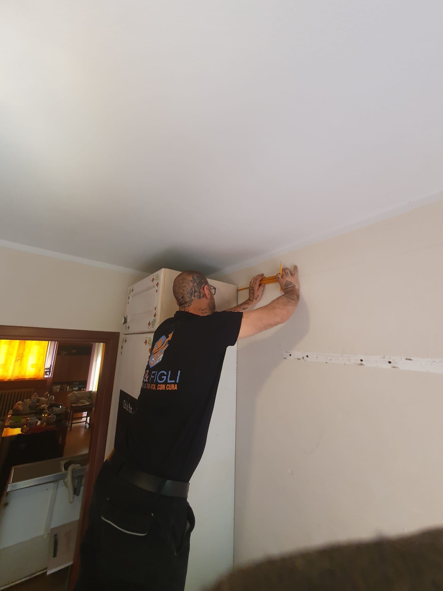 Una persona sta installando delle modanature vicino al soffitto di una stanza, allungandosi accanto a un mobile.