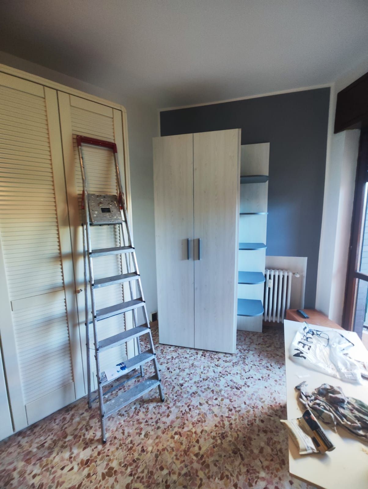 Piccola camera da letto con armadio, scala, sedia e un letto parzialmente visibile sulla destra.