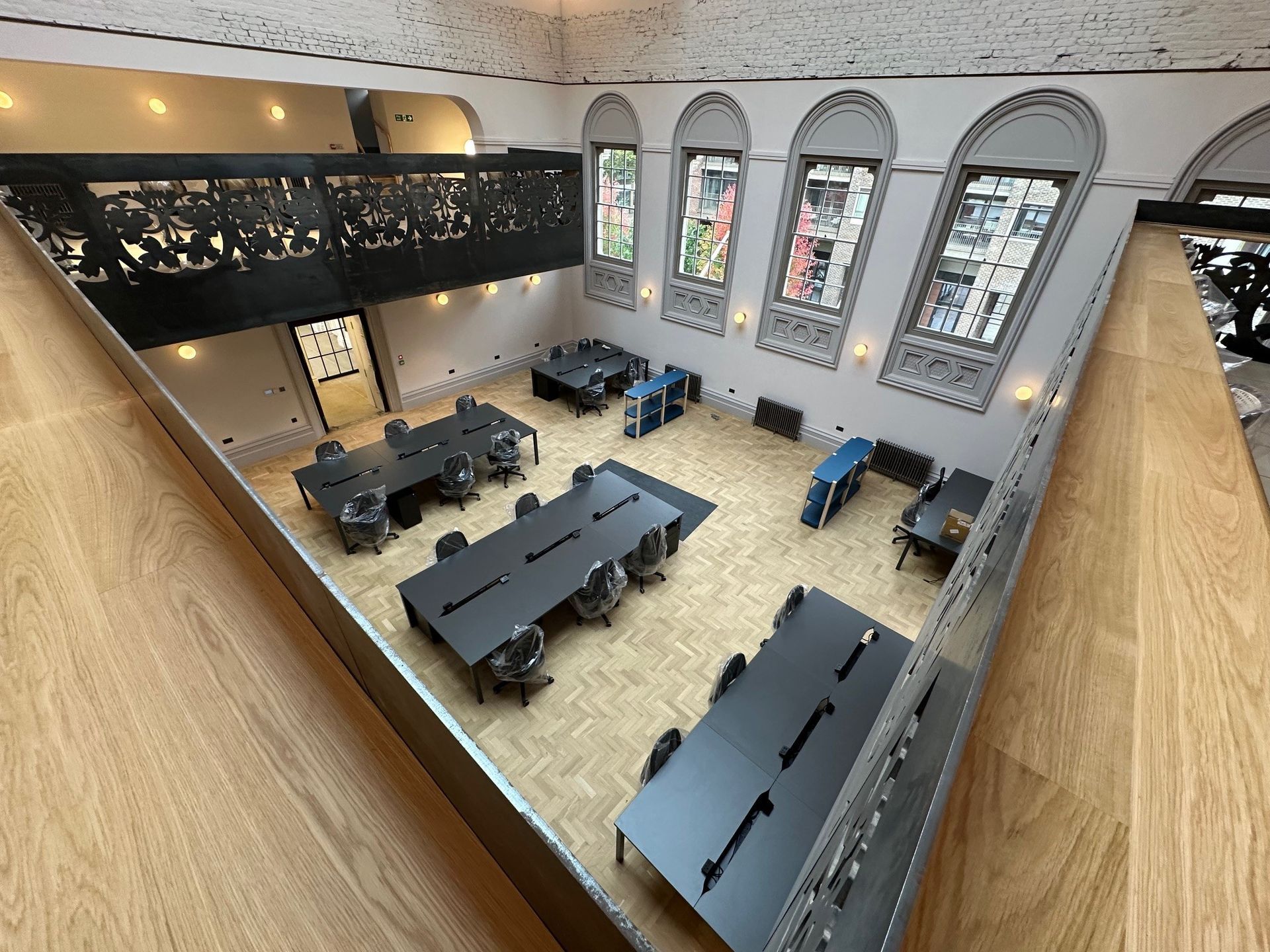 view from a ornate balcony looking down on to dark meeting tables, a parquet hard wood floor, large ornate arched windows.