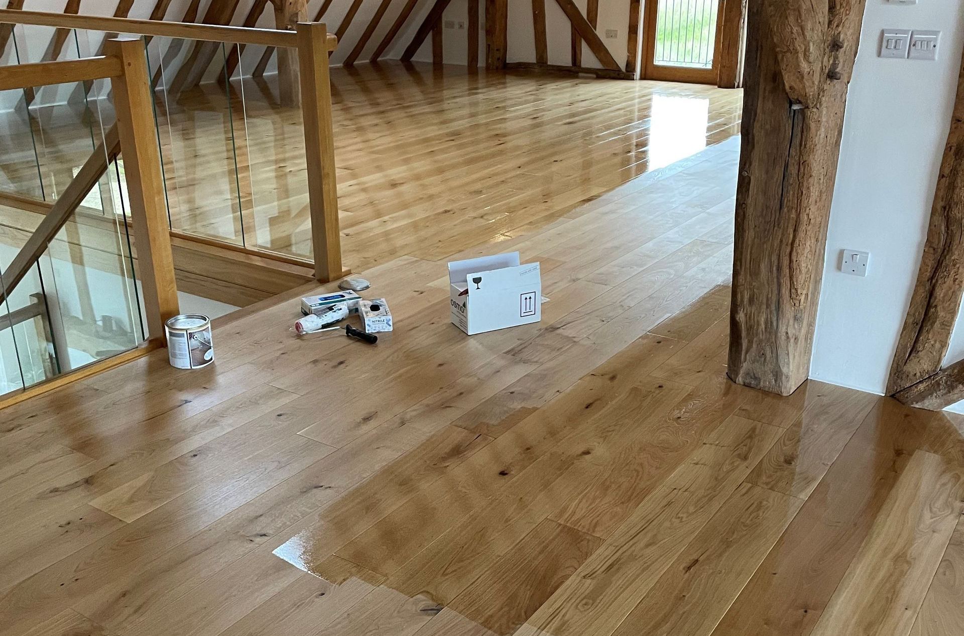 wooden floor with tudor beamed walls and a glass bannister top of a staircase in the background.