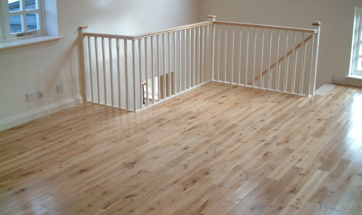 Light wood flooring and white railing enclose a stairway. Sunlight streams in from windows.