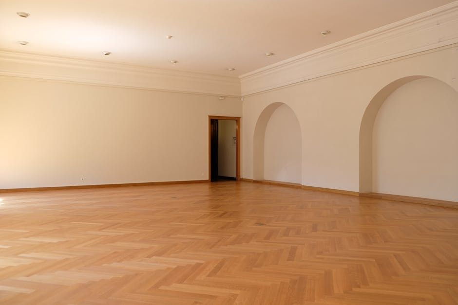 Empty room with light wood parquet floor, white walls, and decorative molding. Arched alcoves on the right wall.