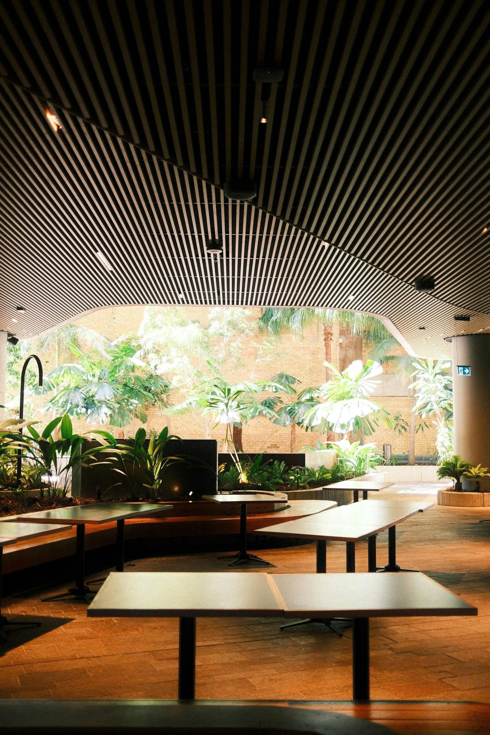 Interior view of a cafe with tables, a striped ceiling, and a large window with greenery.