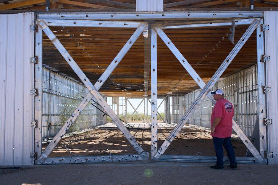 Man standing in front of large open barn doors with a metal X-braced frame. Interior is visible.