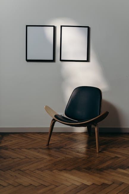 Two framed white spaces above a wooden chair with a dark blue seat, on a wooden parquet floor.