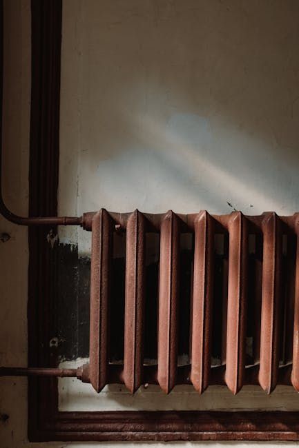 Rusty, vertical radiator against a white wall with dark trim. Sunlight streams across.