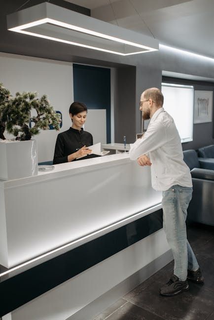 Receptionist assisting a man at a modern white counter in an office.