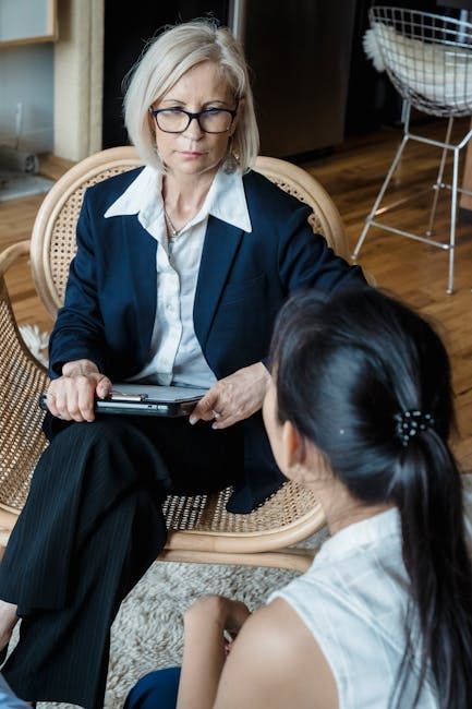 A woman in a suit consults with another woman seated in front of her. They are indoors.