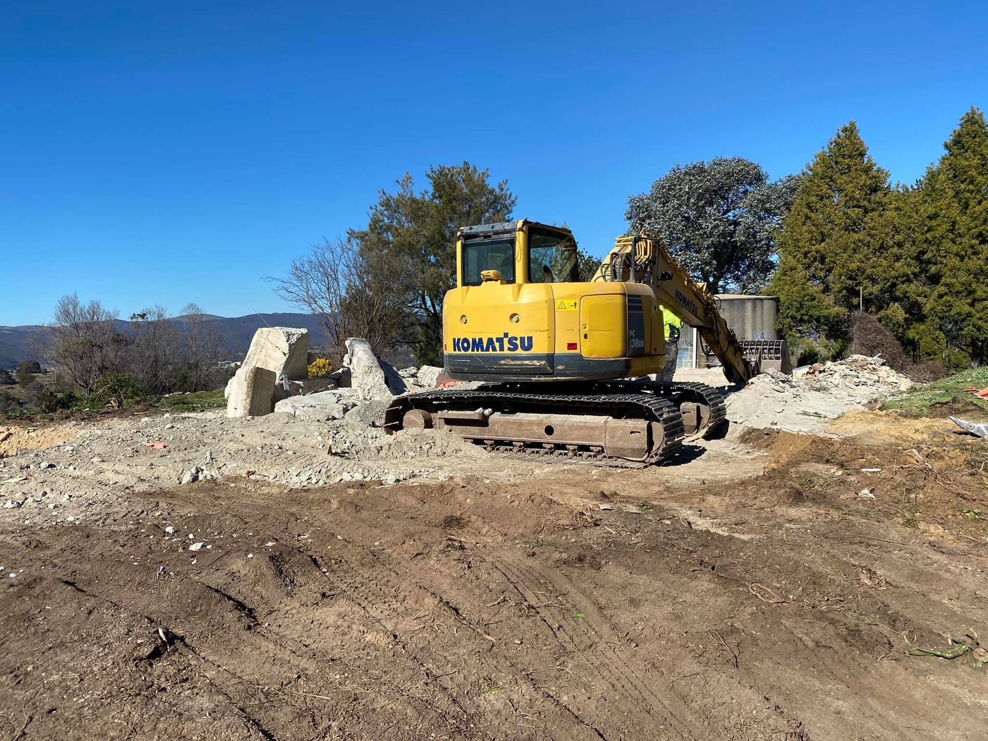 Yellow Komatsu excavator on construction site clearing debris. Sunny, outdoor scene. — Brucic Construction in Dickson, ACT
