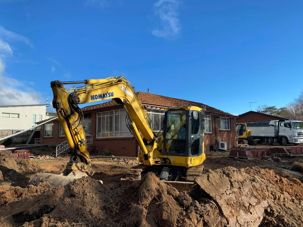 Yellow excavator digging near a brick house on a sunny day. — Brucic Construction in Dickson, ACT
