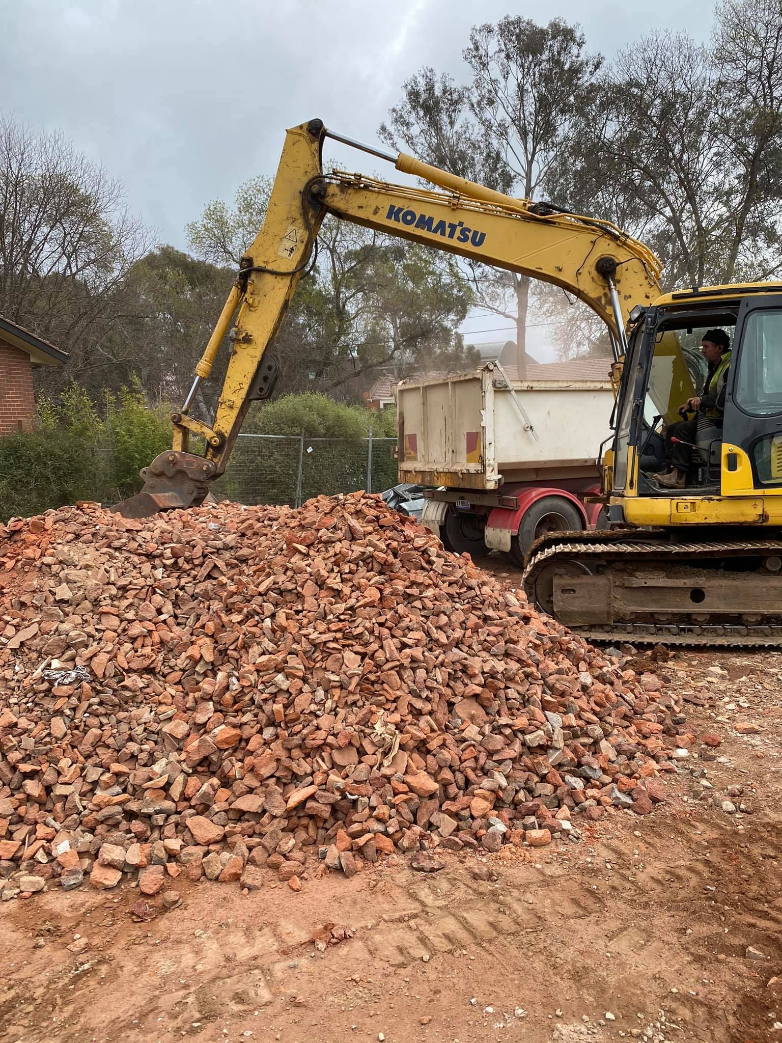 Yellow Komatsu Excavator Loading Brick Debris Into a Truck — Brucic Construction in Goulburn, NSW