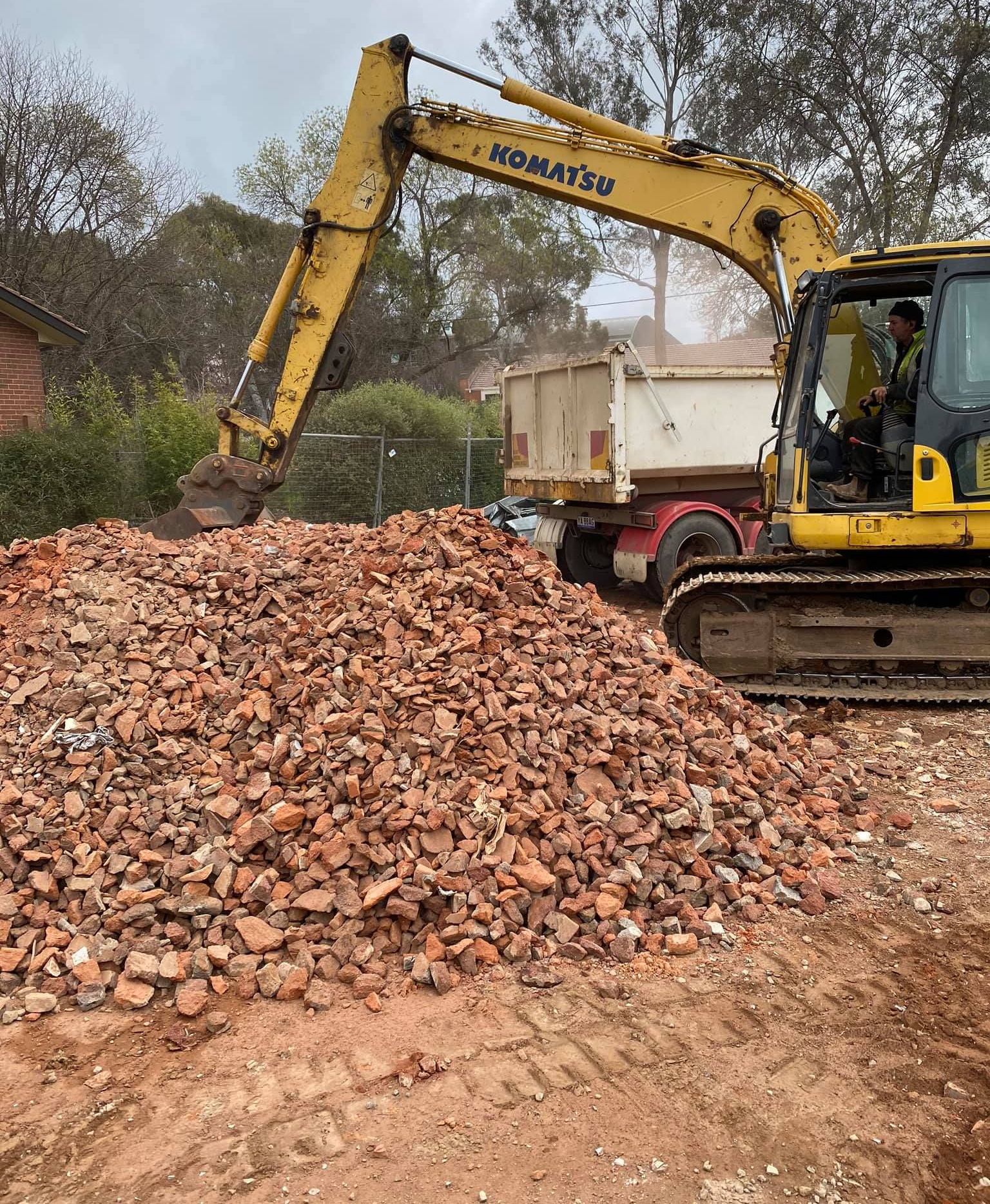 Yellow excavator loading brick rubble into a truck at a construction site. — Brucic Construction in Dickson, ACT