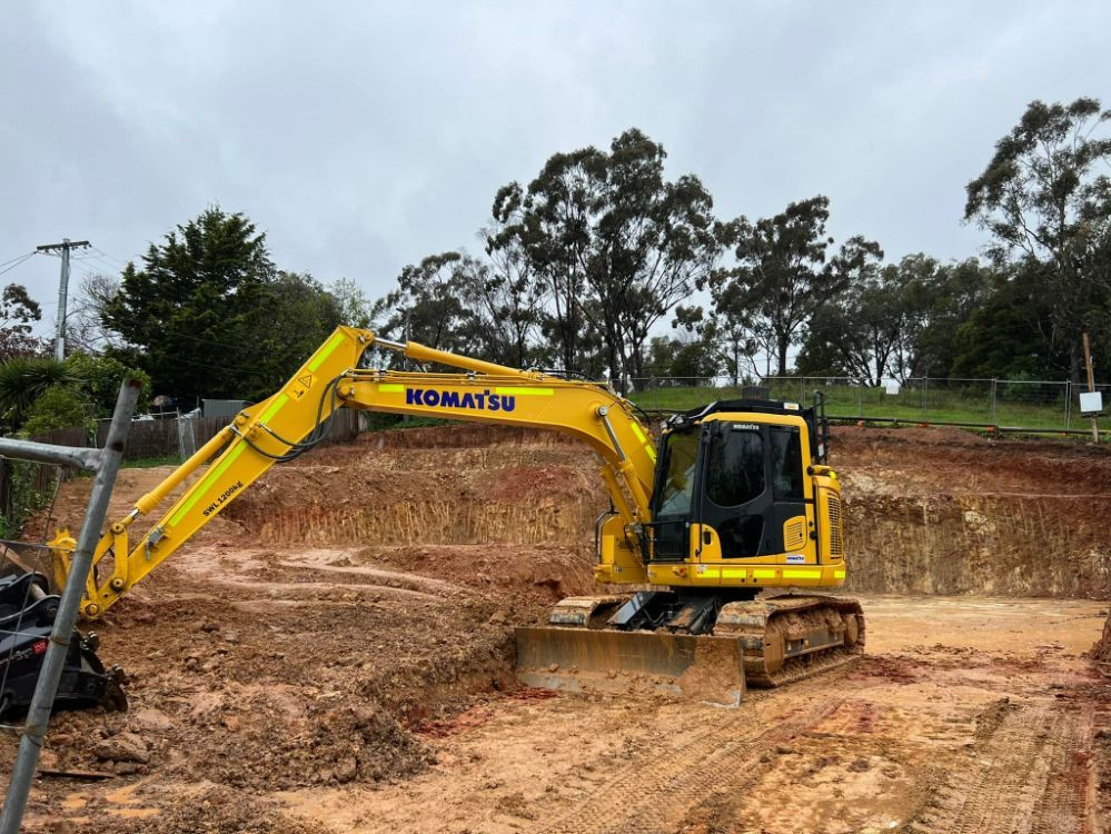 Yellow Komatsu Excavator on a Muddy Construction Site, Digging Into Reddish Earth — Brucic Construction in Dickson, ACT