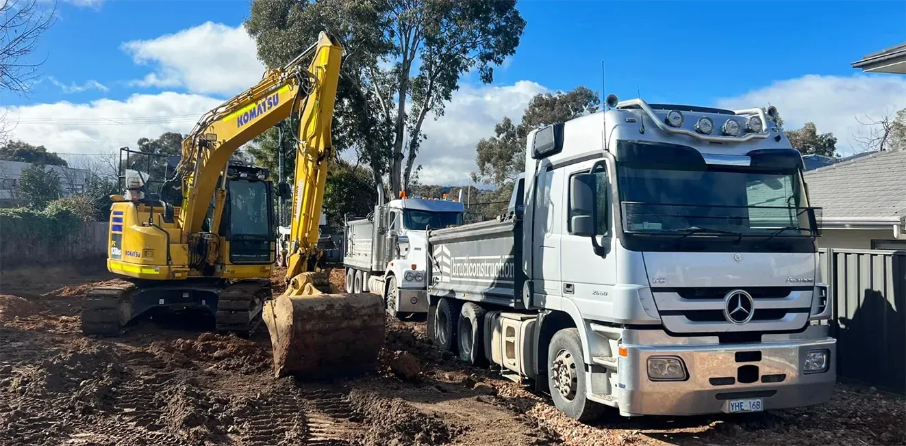 Yellow Excavator Loading Dirt Into a Truck at a Construction Site — Brucic Construction in Dickson, ACT