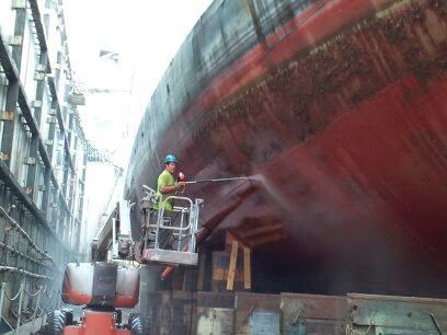 A man is cleaning a large red ship in a dock.