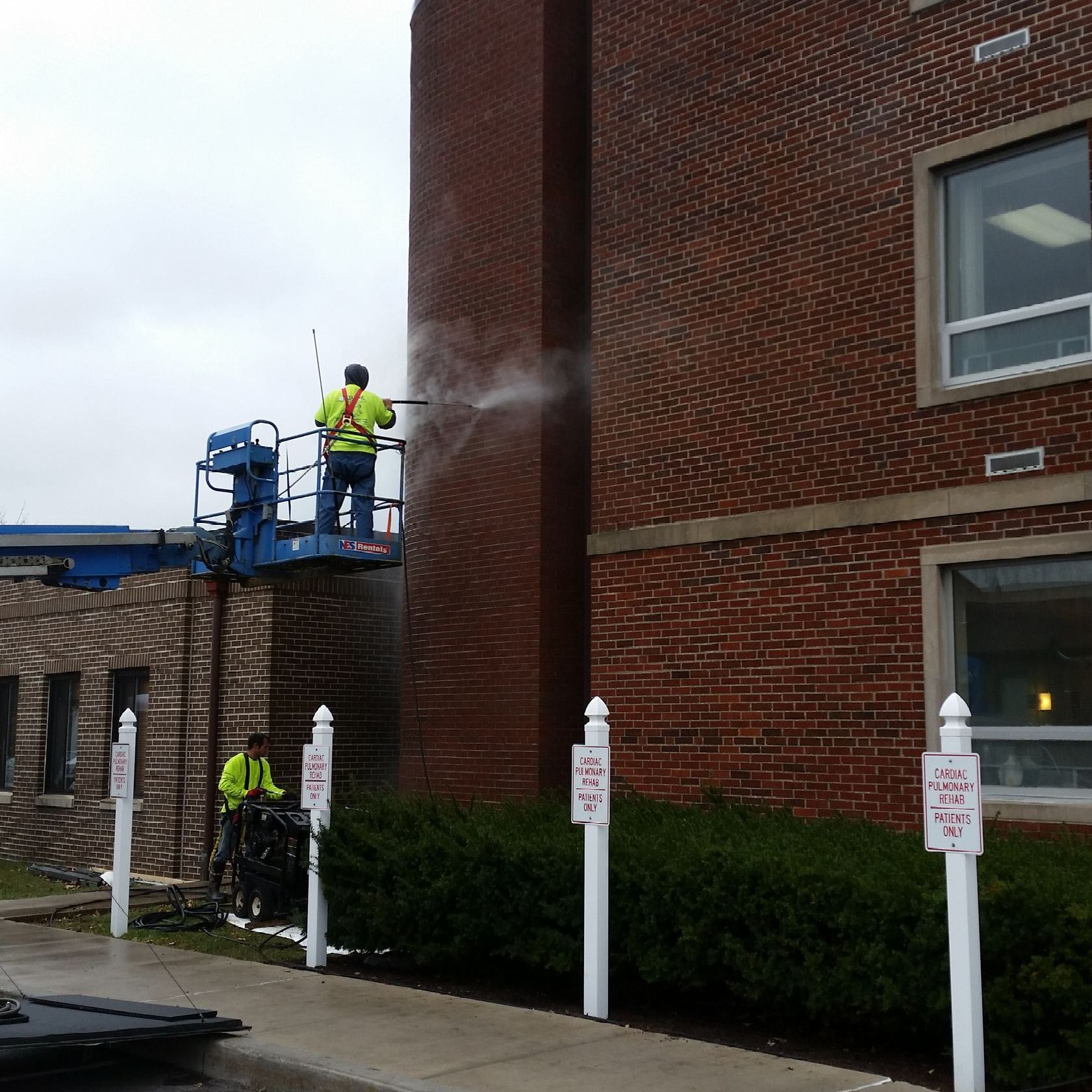A man is cleaning a brick building with a high pressure washer