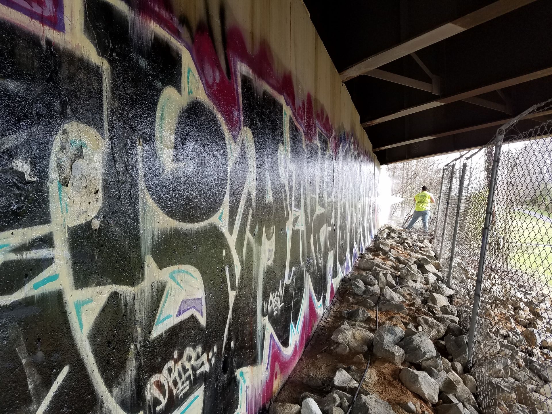 A person is standing under a bridge with graffiti on the wall.