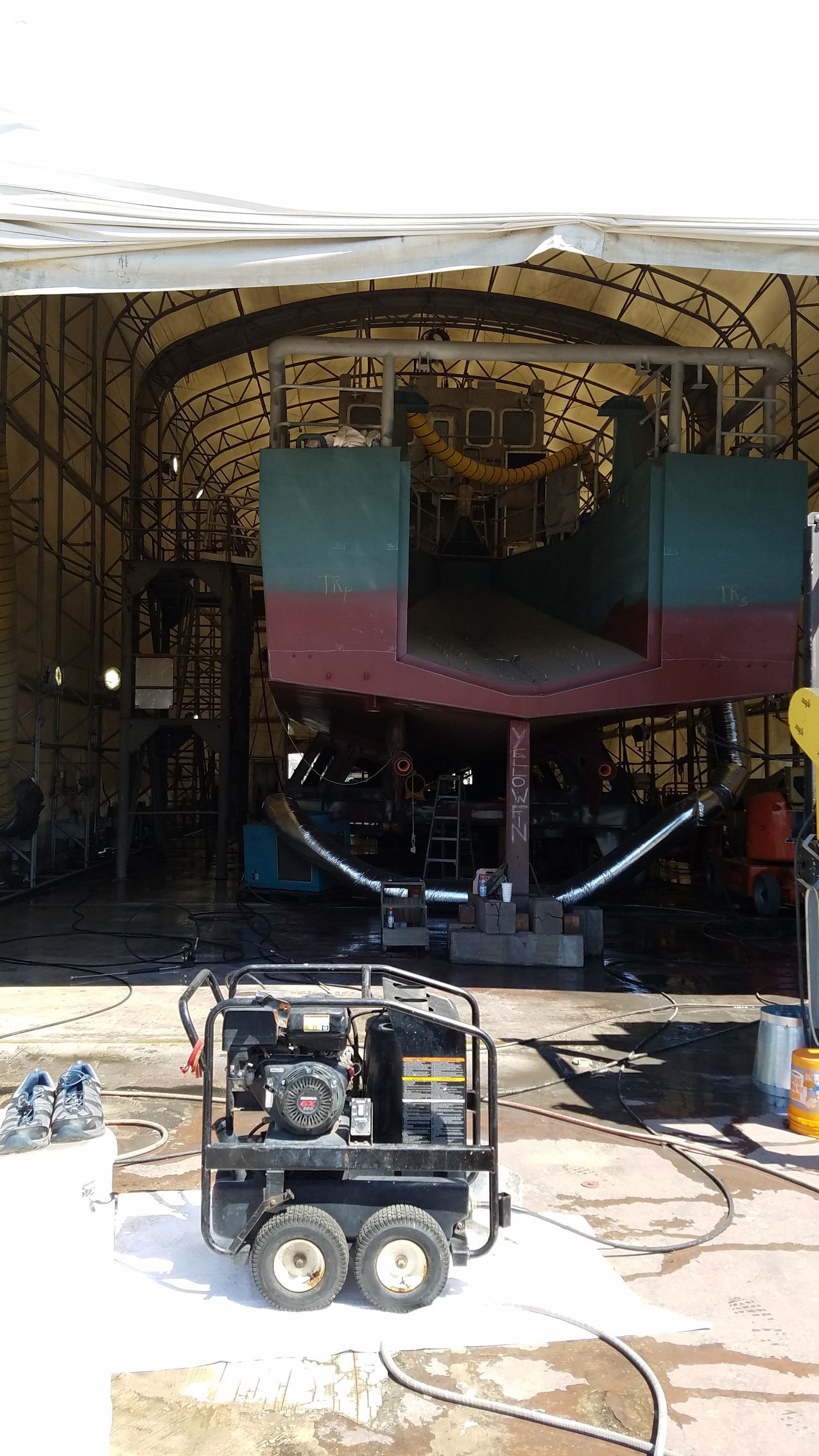 A boat is being worked on in a garage with a machine in front of it.