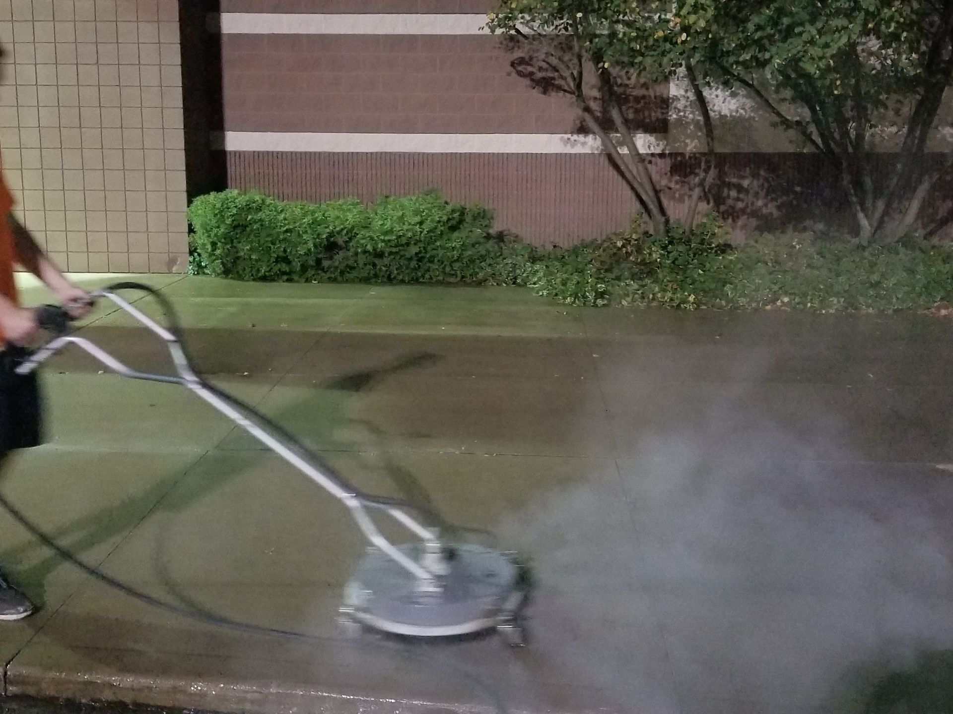 A man is using a pressure washer to clean a sidewalk.