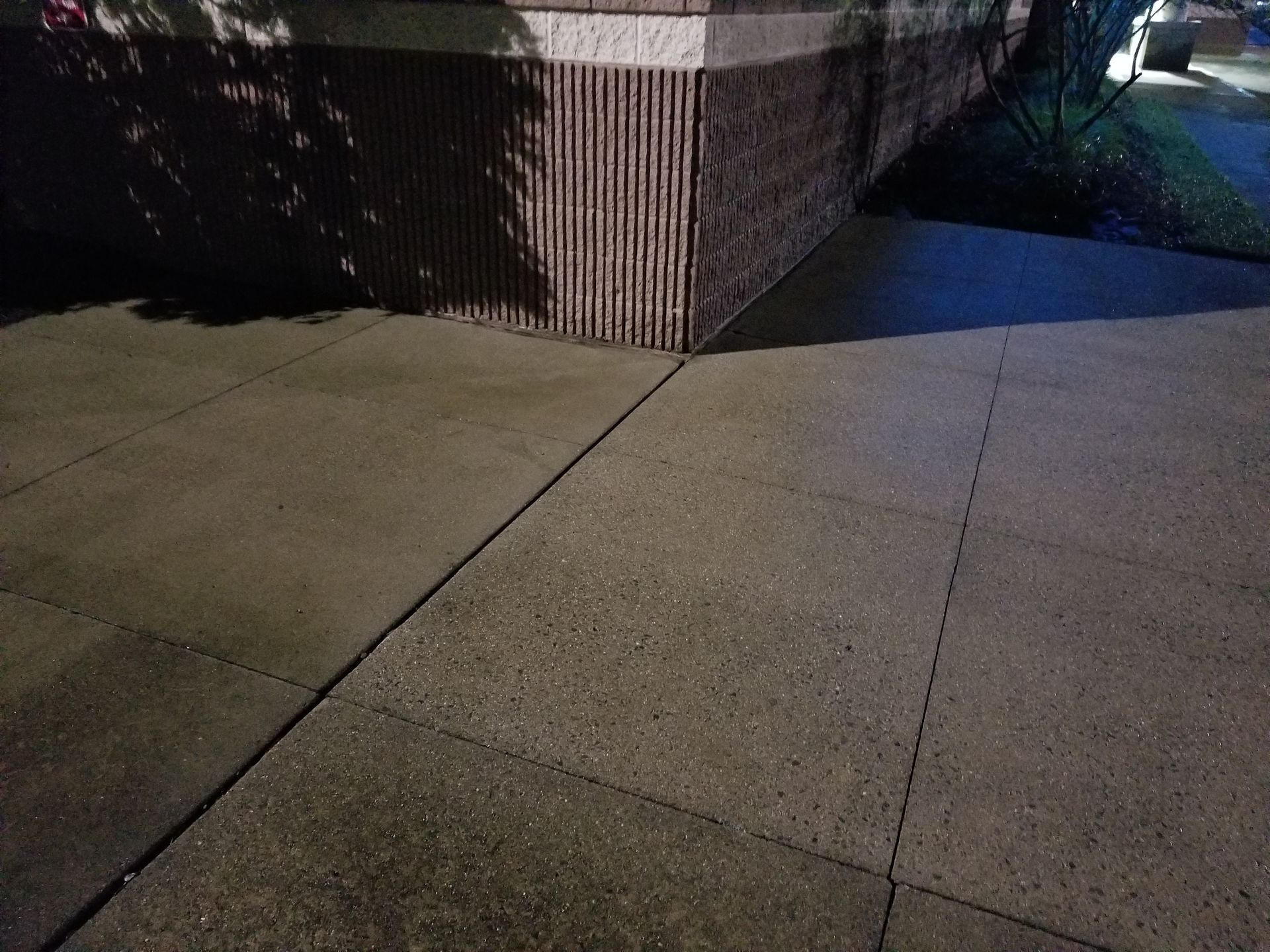 A sidewalk with a brick wall in the background at night