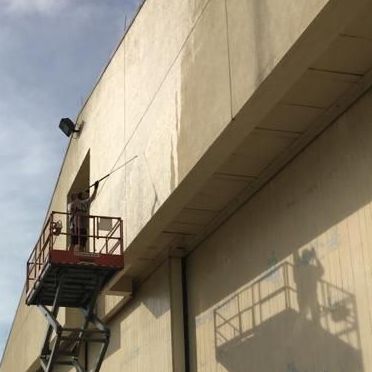 A man is cleaning the side of a building on a lift.