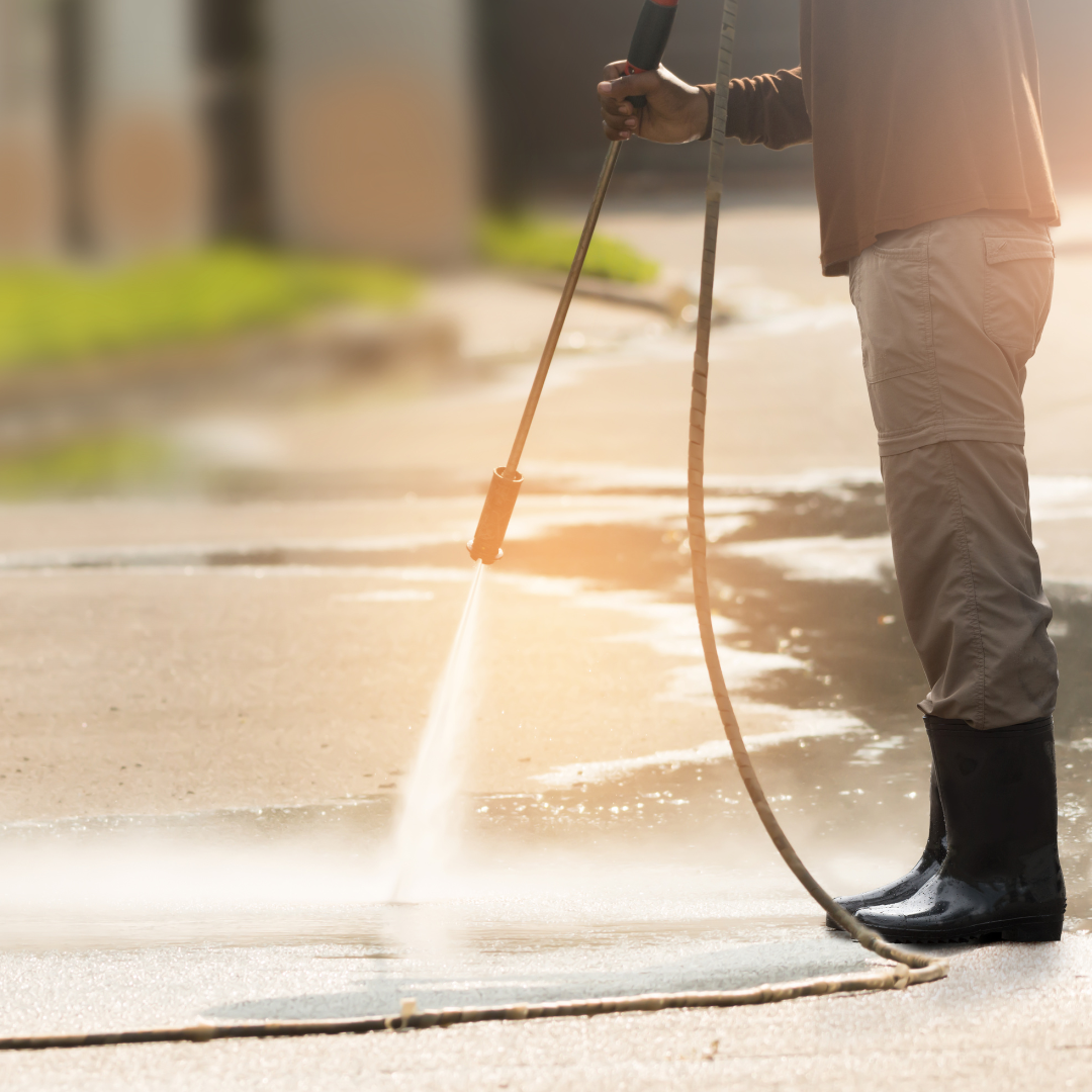 A man is using a high pressure washer to clean the sidewalk.