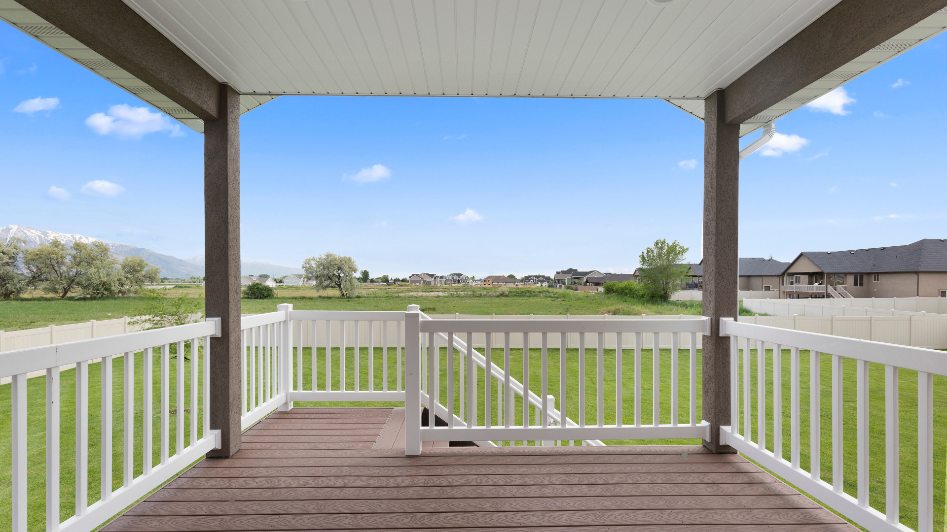An empty porch with a white railing and a view of a field.