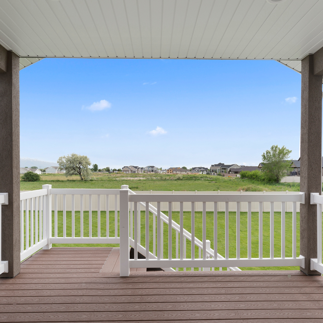 A porch with a white railing overlooking a grassy field