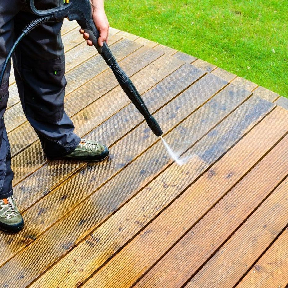 A person is cleaning a wooden deck with a high pressure washer.