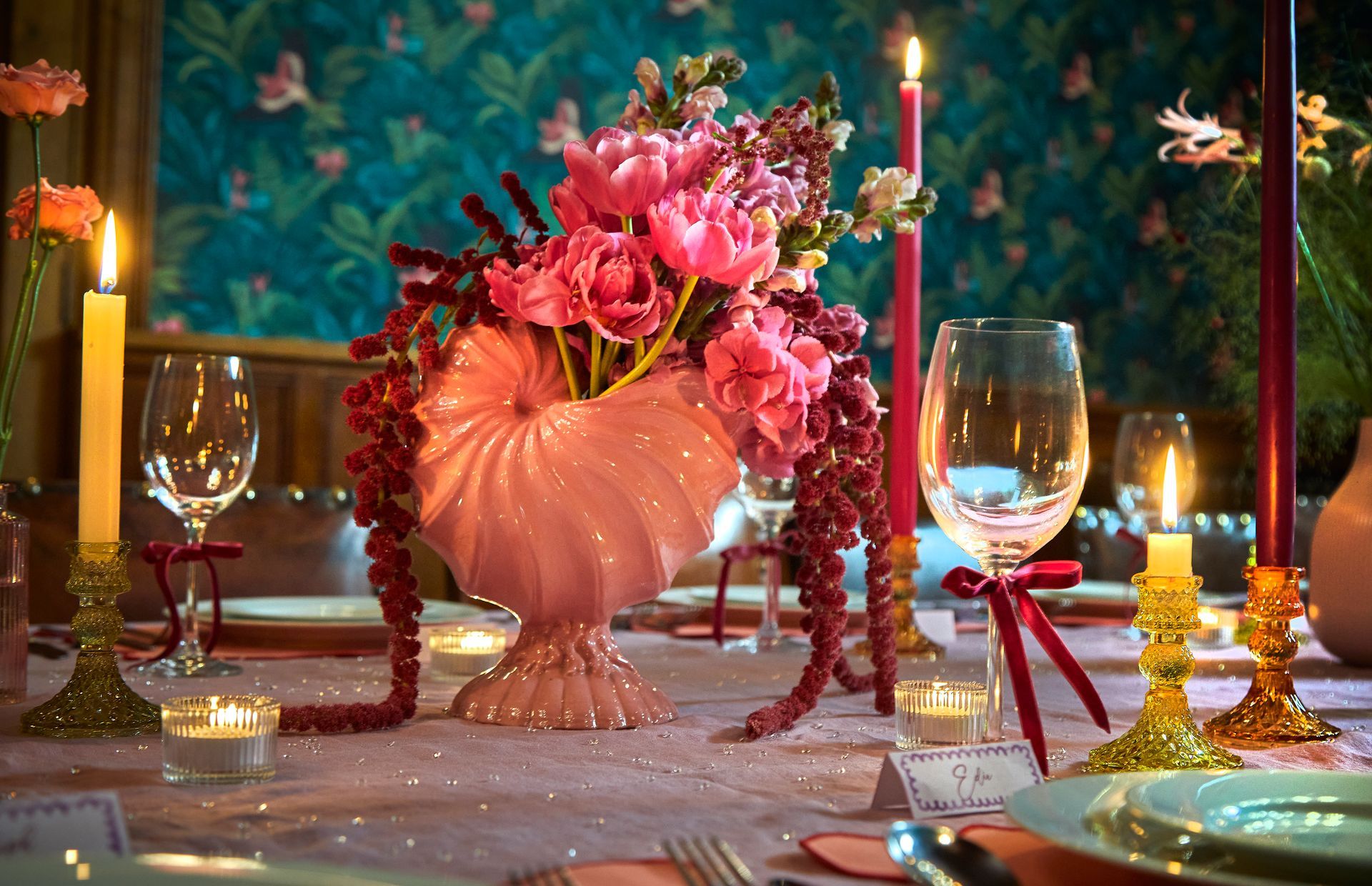 Elegant candlelit table setting with pink floral centerpiece, wine glasses, and gold accents