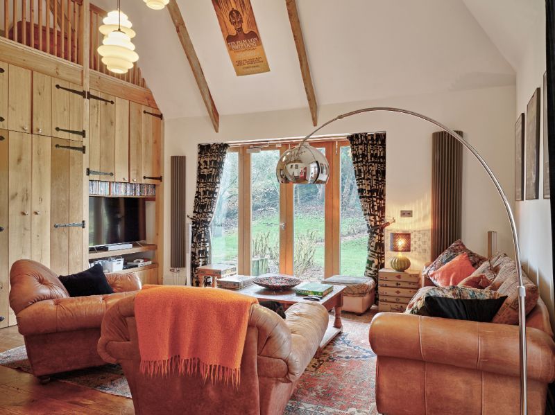 Cozy living room with tan sofas, arched floor lamp, and large windows overlooking trees