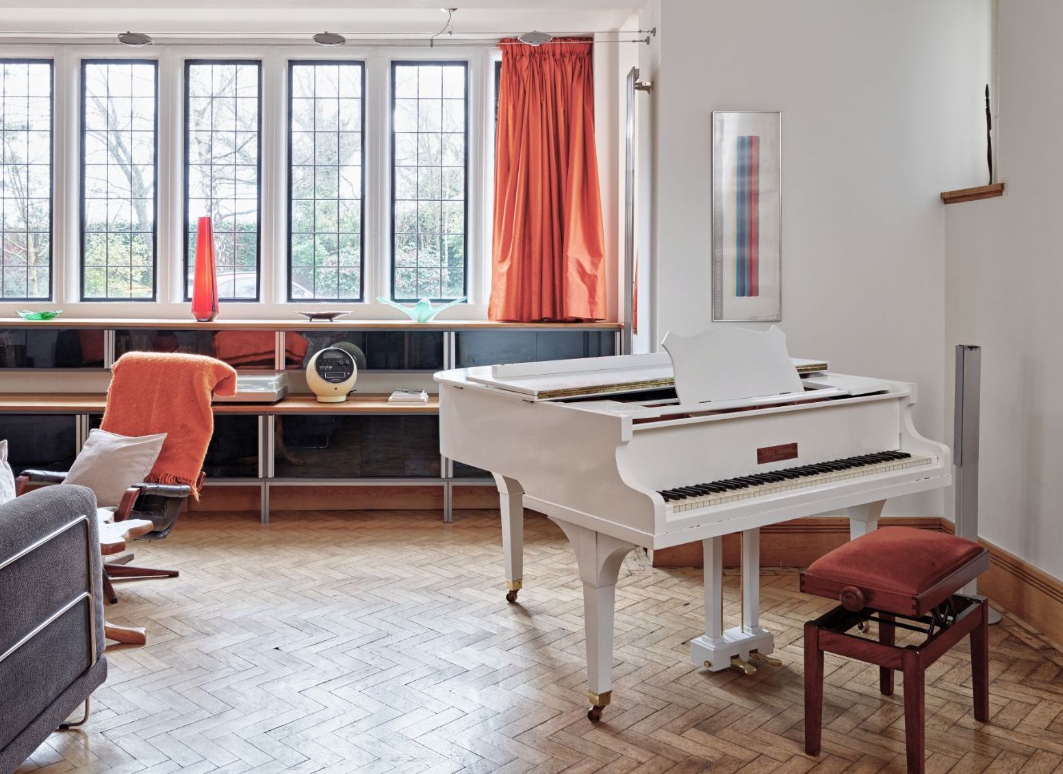 Bright living room with a white piano, orange curtains, and large windows