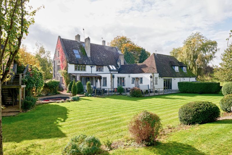Large white countryside house with a red roof and manicured green lawn in a sunny garden